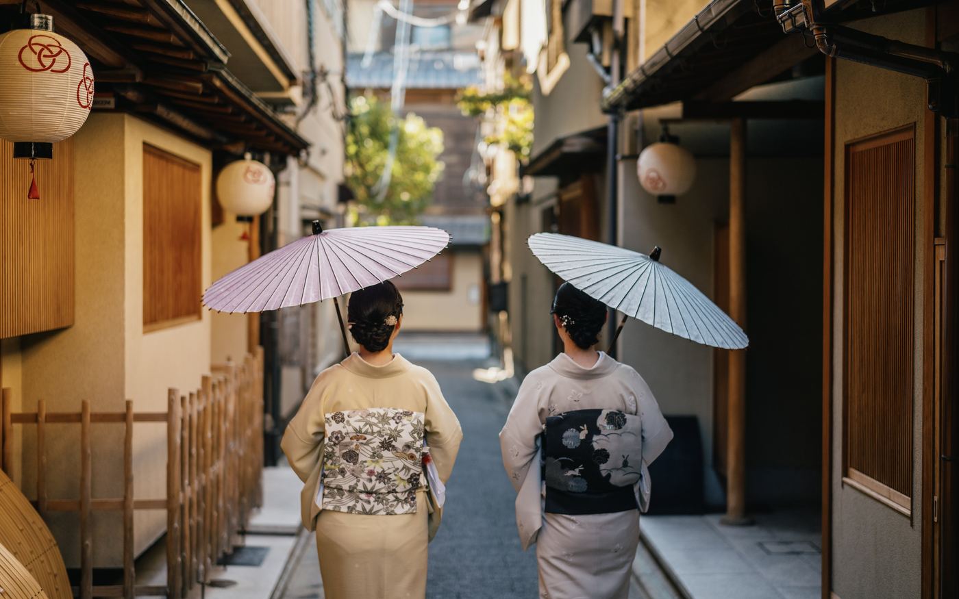 提灯の下がる路地を和傘で歩く着物姿のお二人の後ろ姿