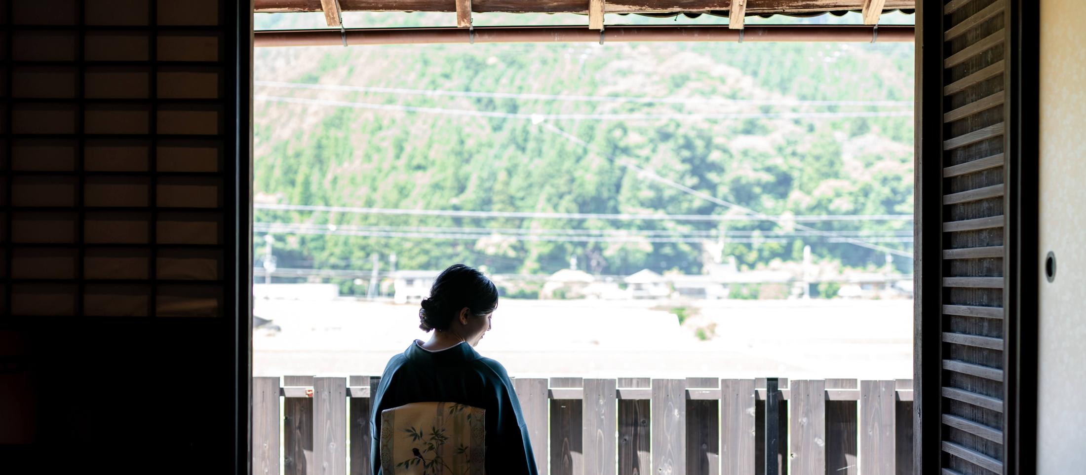 障子越しに川と山を望む座敷に座る正絹の着物姿の女性