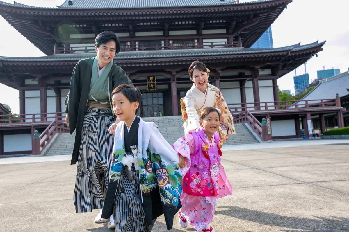 羽織袴の男の子と被布姿の女の子、訪問着の母親と袴の父親が並んで歩く七五三の family