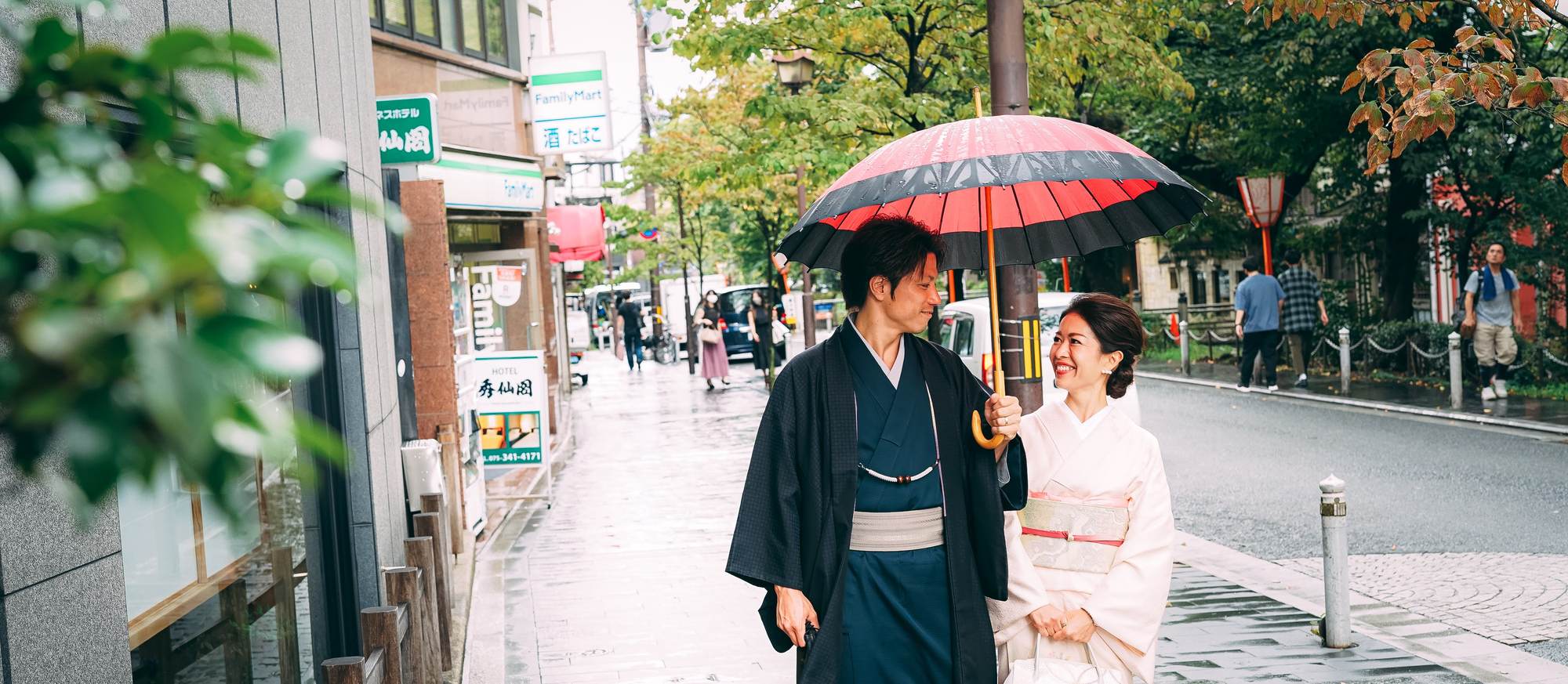 雨の京都の街を赤い和傘で歩く着物姿のカップル