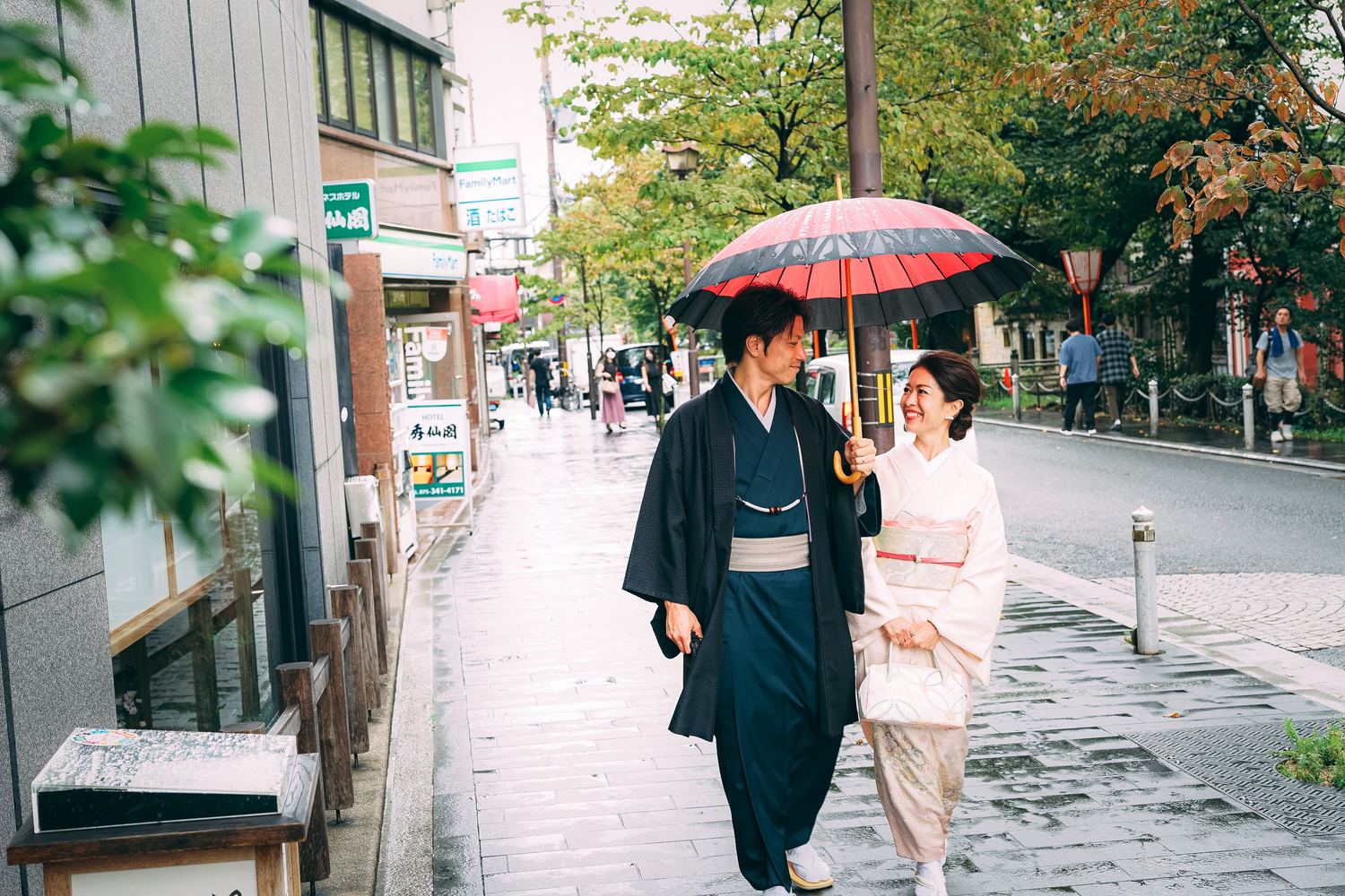 雨の京都の街並みを赤い和傘で歩く着物姿のカップル