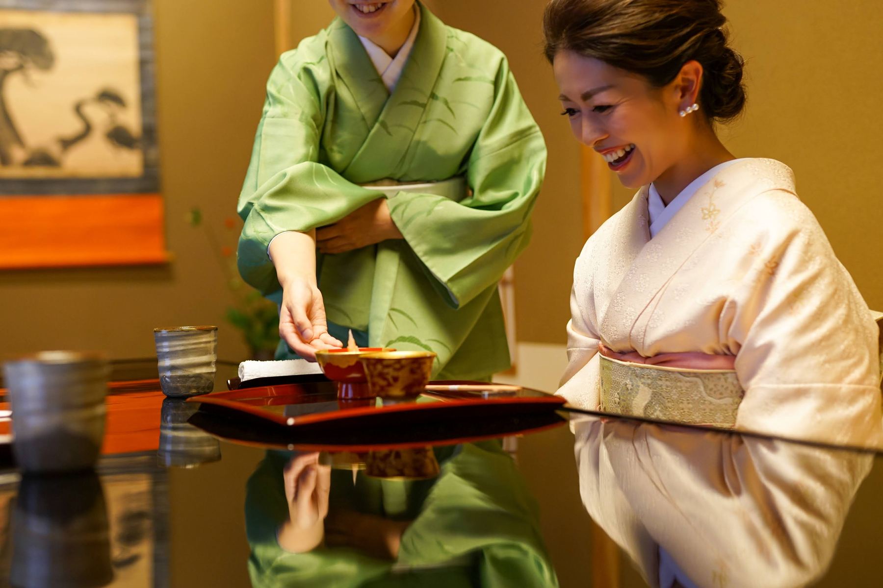 膳を運ぶ緑の着物姿の女将と受け取る女性