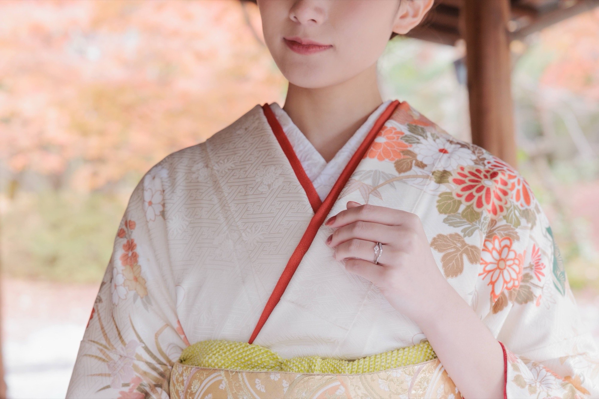 紅葉を背に指輪を添えた訪問着姿の女性